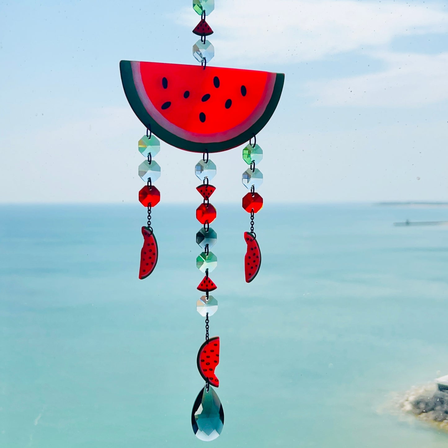 Handmade watermelon-themed suncatcher featuring a large semi-translucent polymer clay watermelon slice with dangling glass crystals and smaller clay watermelon pieces, all suspended from black-plated stainless steel chain