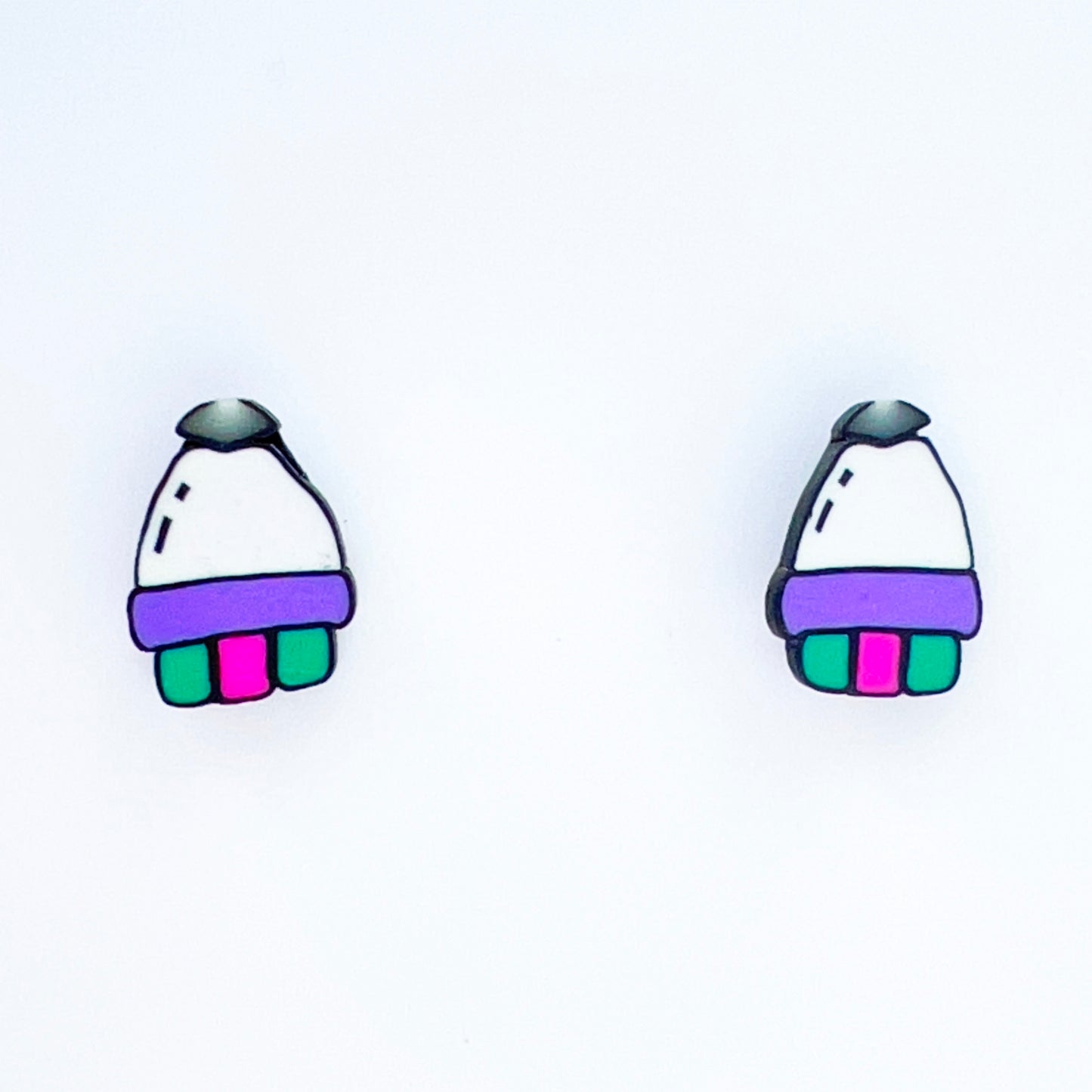 Close-up on pair of handmade polymer clay rocket ship earrings with black nose, white rounded cone, purple. green and pink rockets. Made with titanium posts, featuring a playful space design. Lightweight, hypoallergenic, and one-of-a-kind accessory.