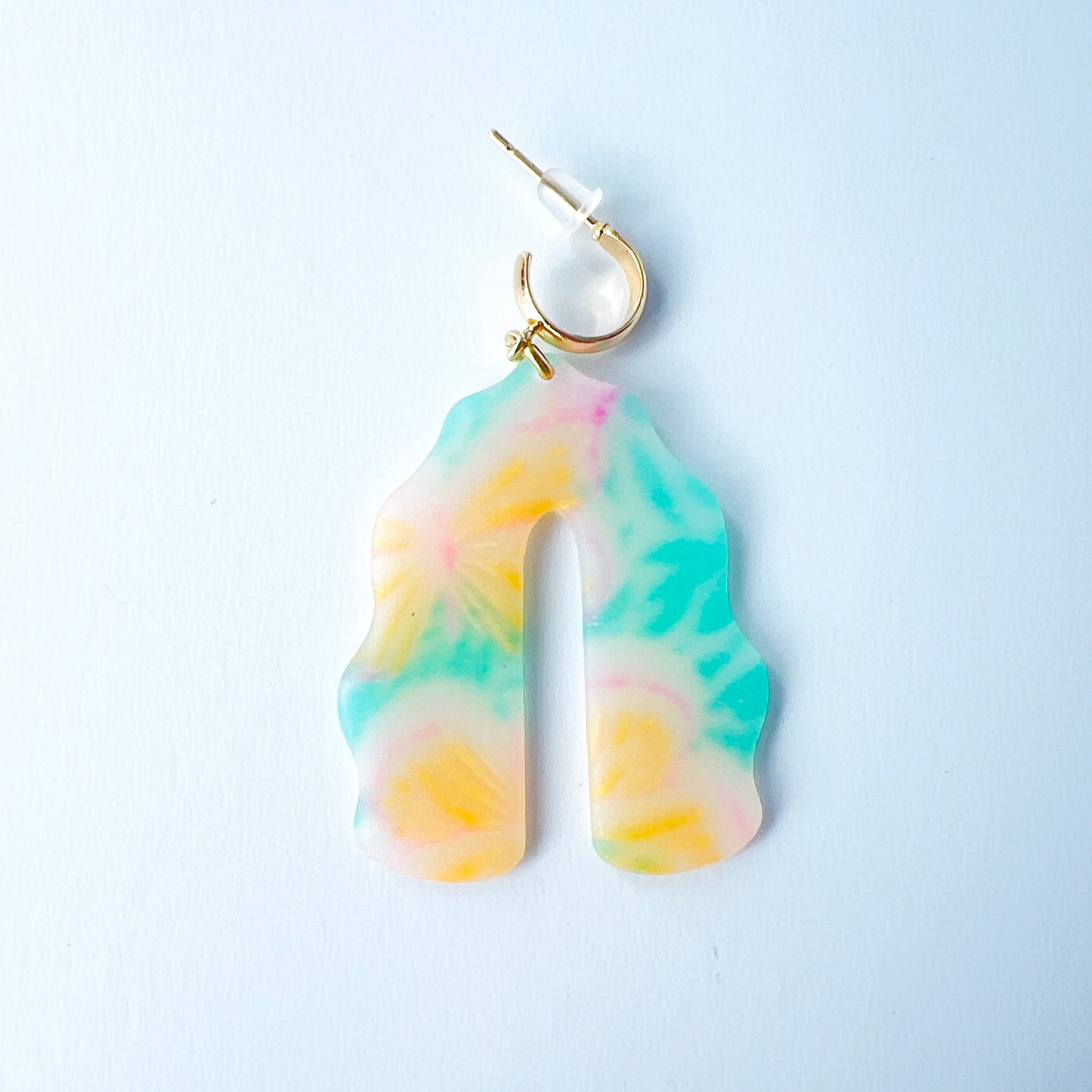 A pair of handmade polymer clay earrings shaped like arches, with swirled pastel colors and subtle details of yellow butterflies and green leafy accents. The semi-transparent clay design is paired with shiny gold-plated brass half hoop posts.