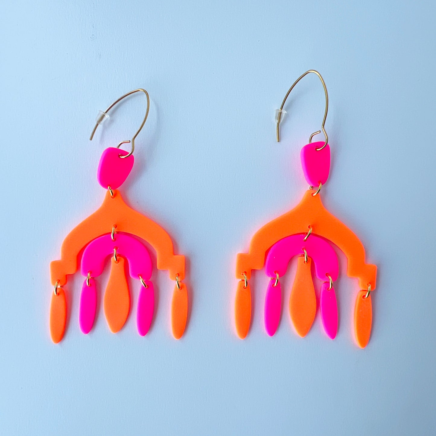 A pair of vibrant handmade chandelier earrings with hot pink and neon orange polymer clay components, featuring multiple dangling shapes on gold-plated stainless steel earwires.
