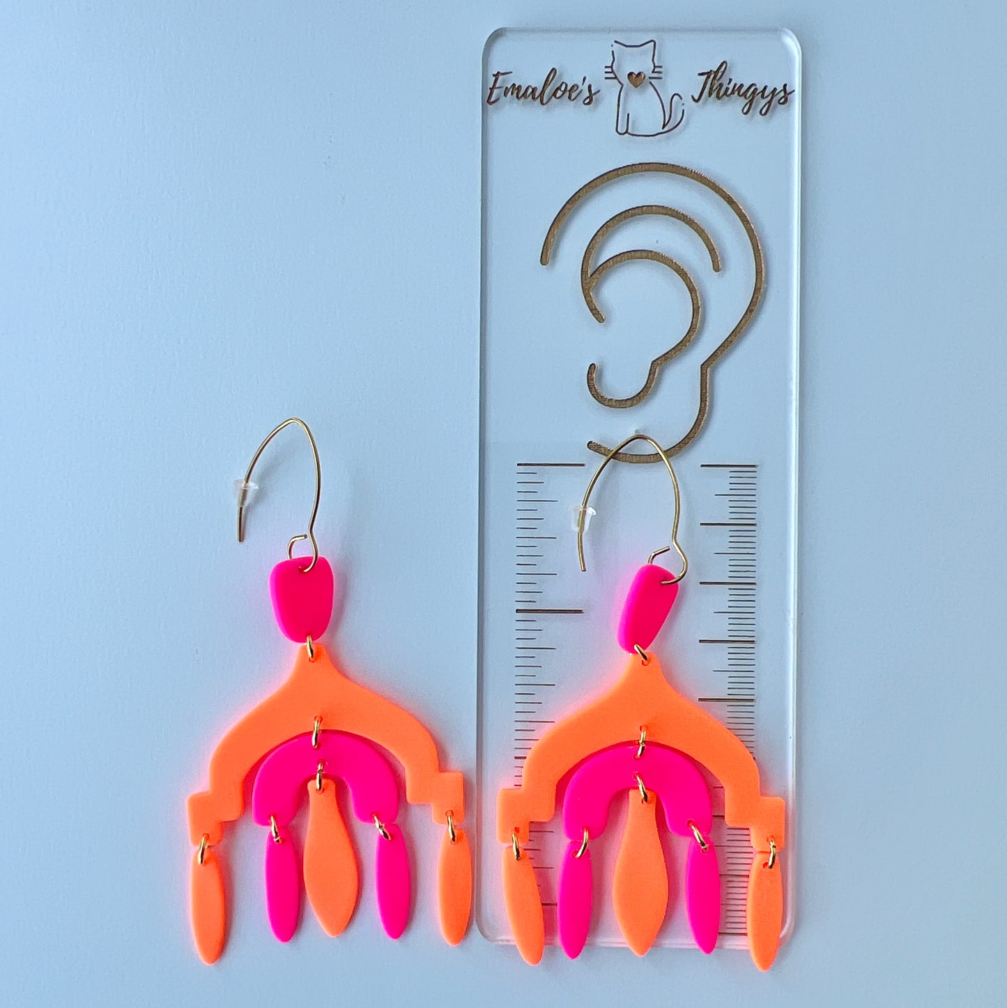 A pair of vibrant handmade chandelier earrings with hot pink and neon orange polymer clay components, featuring multiple dangling shapes on gold-plated stainless steel earwires.