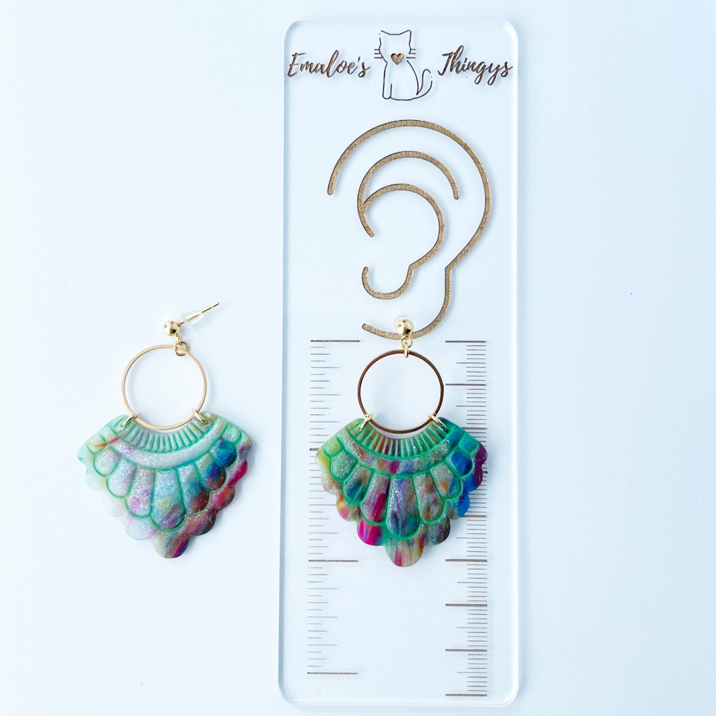 A pair of handmade fan-shaped polymer clay earrings displayed on a white background. The earrings feature gold-plated ball posts and hoops, with semi-transparent rainbow-colored clay and green etched fan-like lines. The marbling effect shows swirls of pink, blue, green, orange, and white.