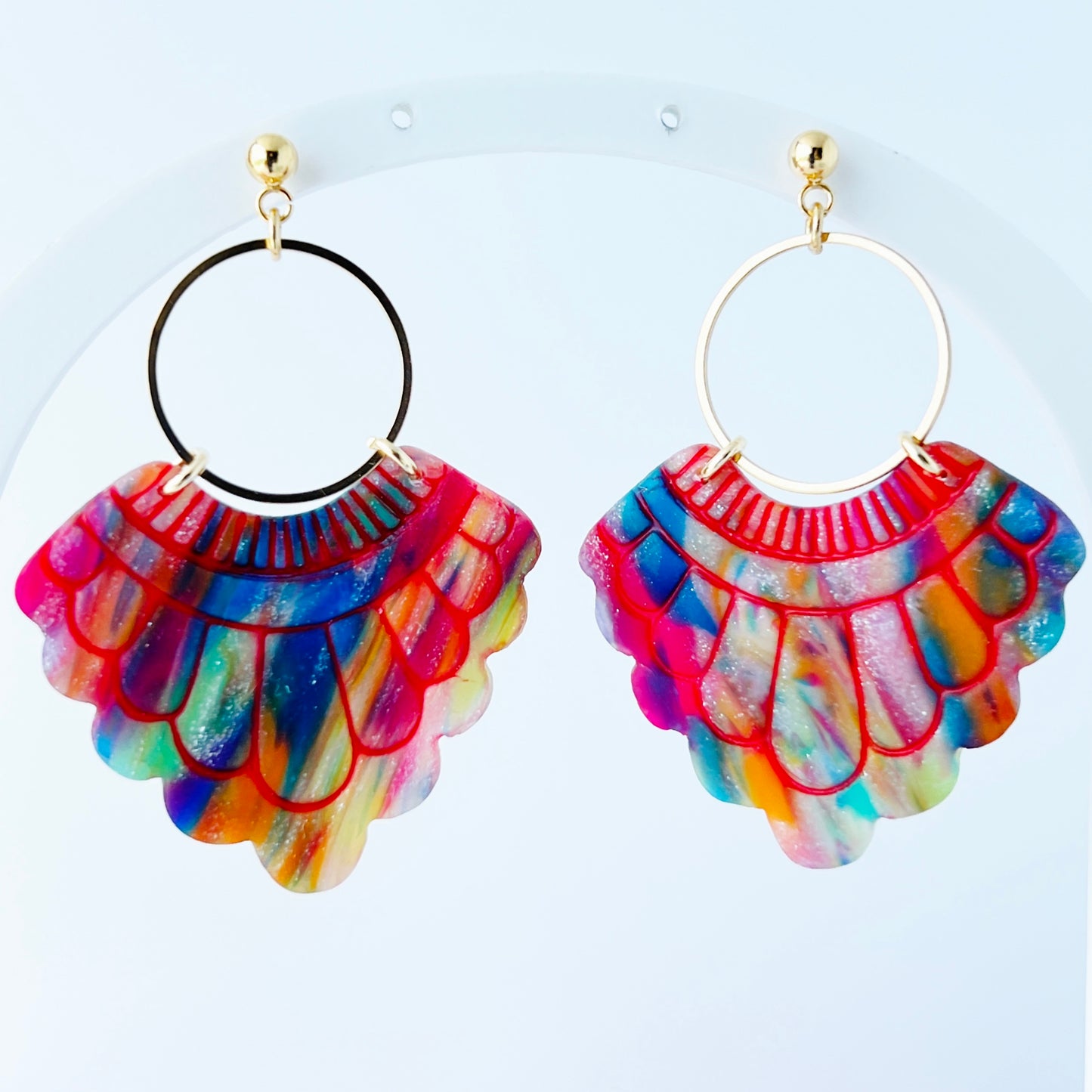 A pair of handmade fan-shaped polymer clay earrings displayed on a white background. The earrings feature gold-plated ball posts and hoops, with semi-transparent rainbow-colored clay and red etched fan-like lines. The marbling effect shows swirls of pink, blue, green, orange, and white.