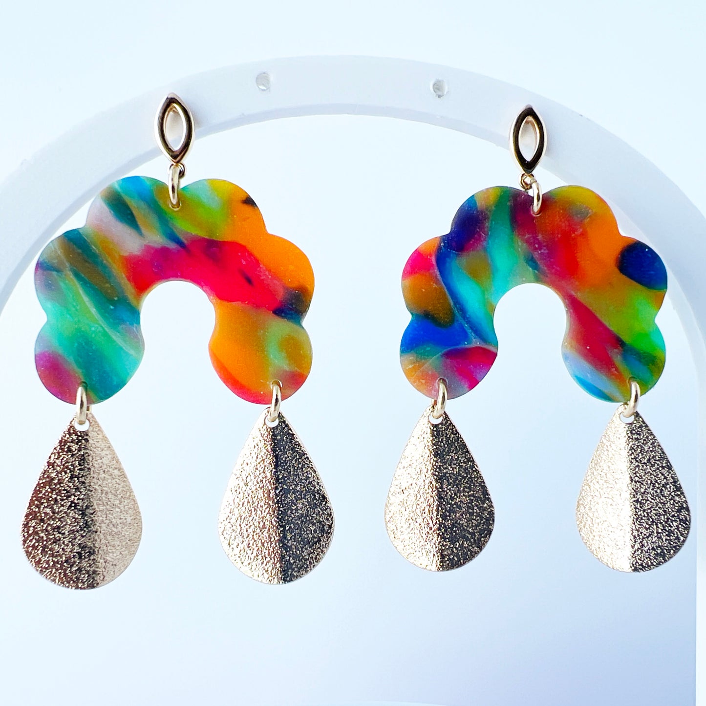 Bold handmade earrings with abstract rainbow swirl polymer clay tops in a semi-translucent finish, featuring glitter-textured gold teardrop dangles and 18K gold-plated brass oval stud posts