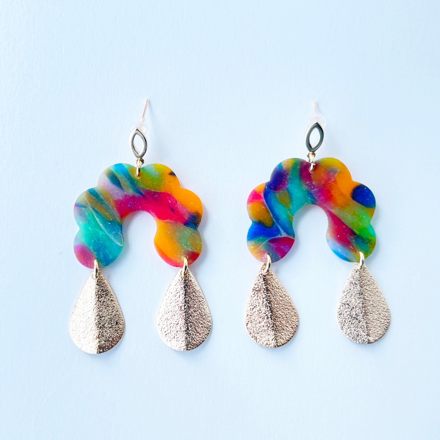 Bold handmade earrings with abstract rainbow swirl polymer clay tops in a semi-translucent finish, featuring glitter-textured gold teardrop dangles and 18K gold-plated brass oval stud posts