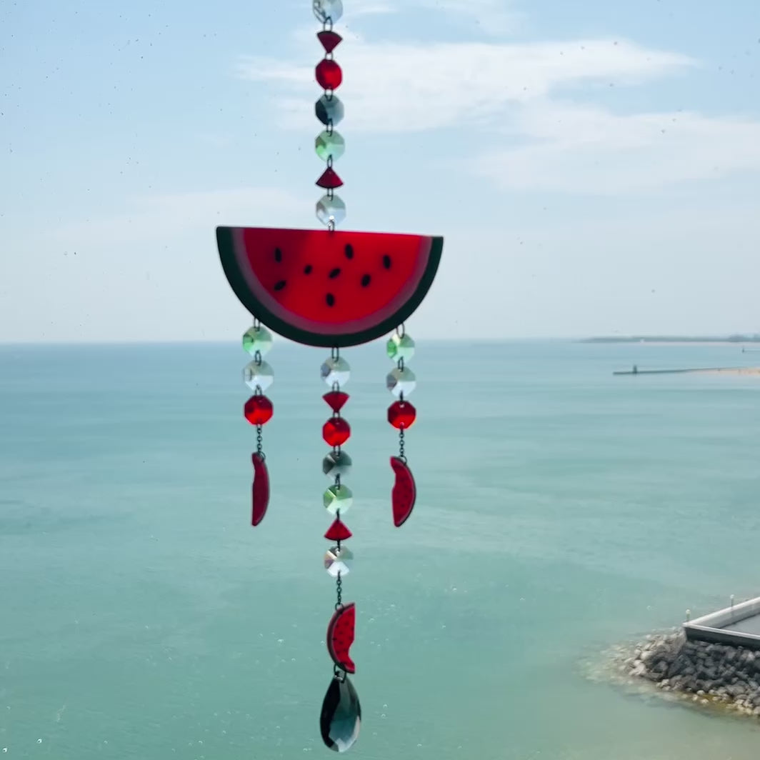 Video of a Handmade watermelon-themed suncatcher featuring a large semi-translucent polymer clay watermelon slice with dangling glass crystals and smaller clay watermelon pieces, all suspended from black-plated stainless steel chain