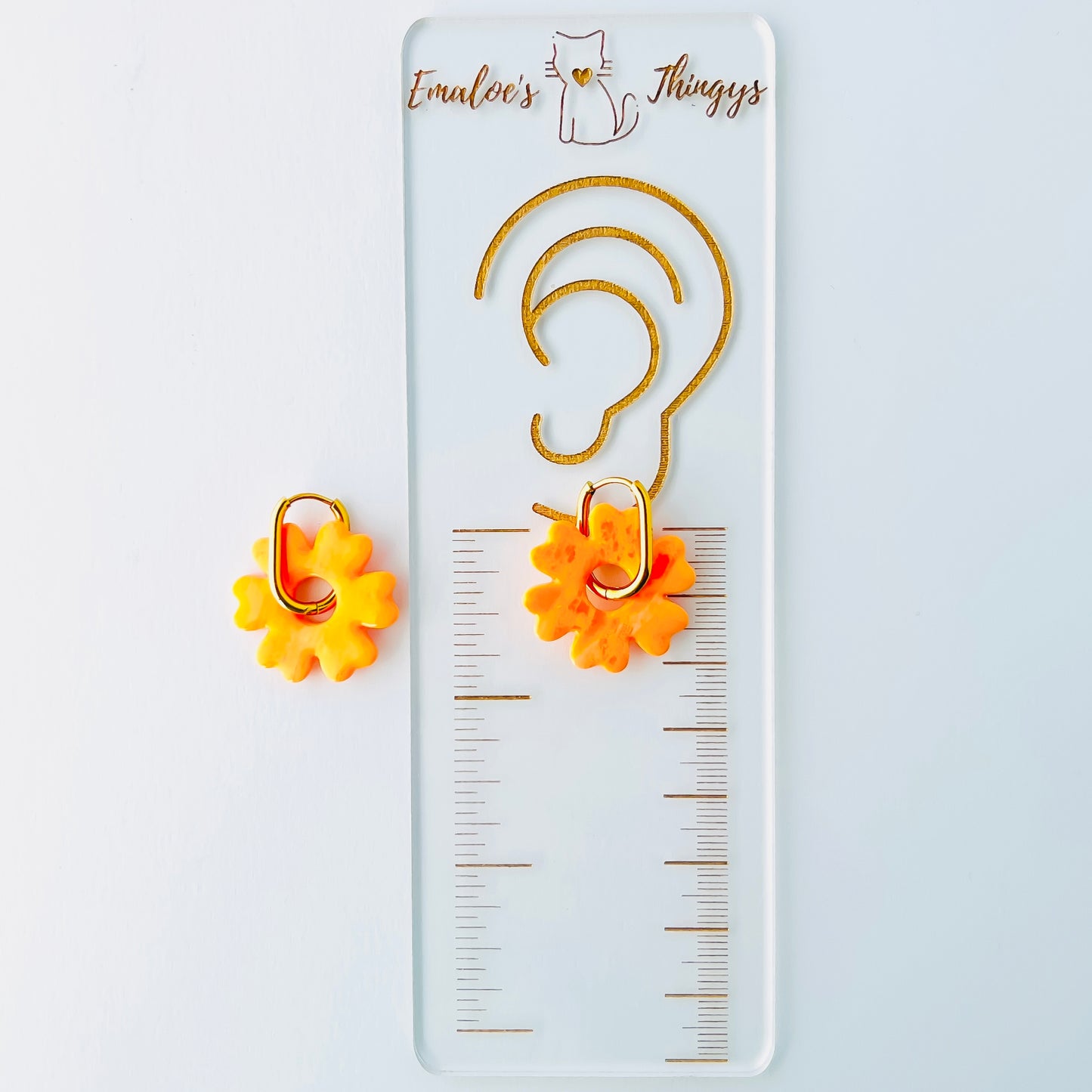 Orange flower-shaped earrings with gold hoops on a white background with a branded Emaloe's Thingys ruler showing the length of the earrings at about 1.25 inches