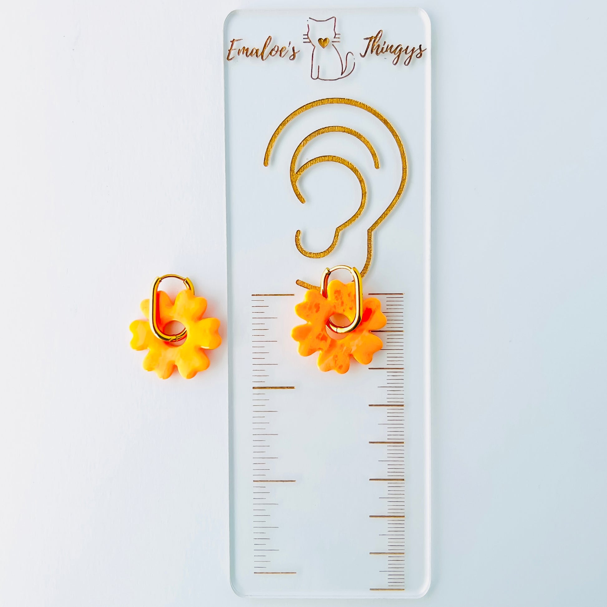 Orange flower-shaped earrings with gold hoops on a white background with a branded Emaloe's Thingys ruler showing the length of the earrings at about 1.25 inches