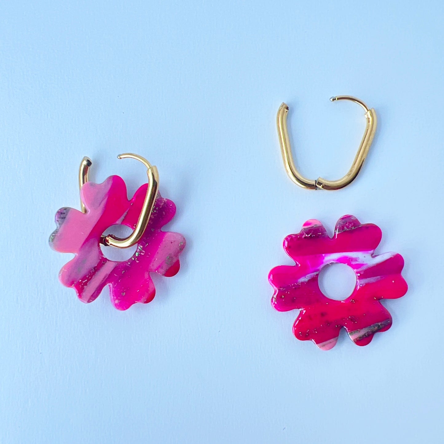 A pair of bold pink handmade polymer clay earrings shaped like abstract flowers, each dangling from a gold oval-shaped 316L stainless steel hoop. One half of the photo shows the hoops worn with the flower, and another shows the flower removed to demonstrate the 2-in-1 styling option.