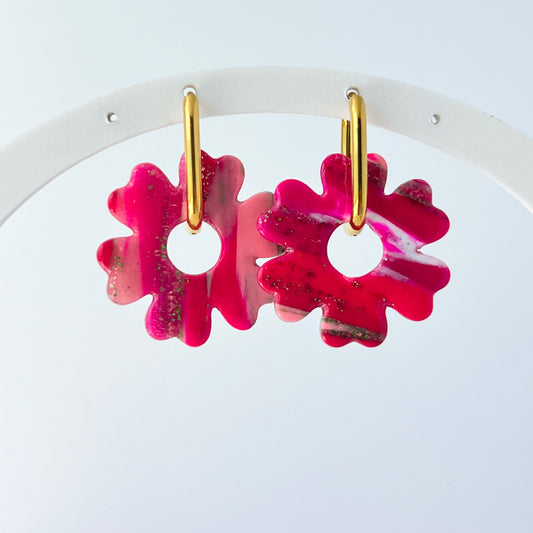 A pair of bold pink handmade polymer clay earrings shaped like abstract flowers, each dangling from a gold oval-shaped 316L stainless steel hoop. 