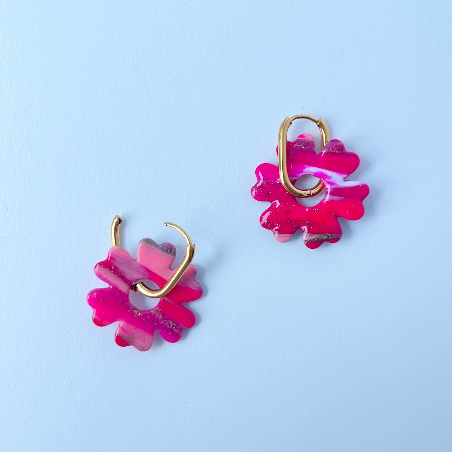 A pair of bold pink handmade polymer clay earrings shaped like abstract flowers, each dangling from a gold oval-shaped 316L stainless steel hoop. 