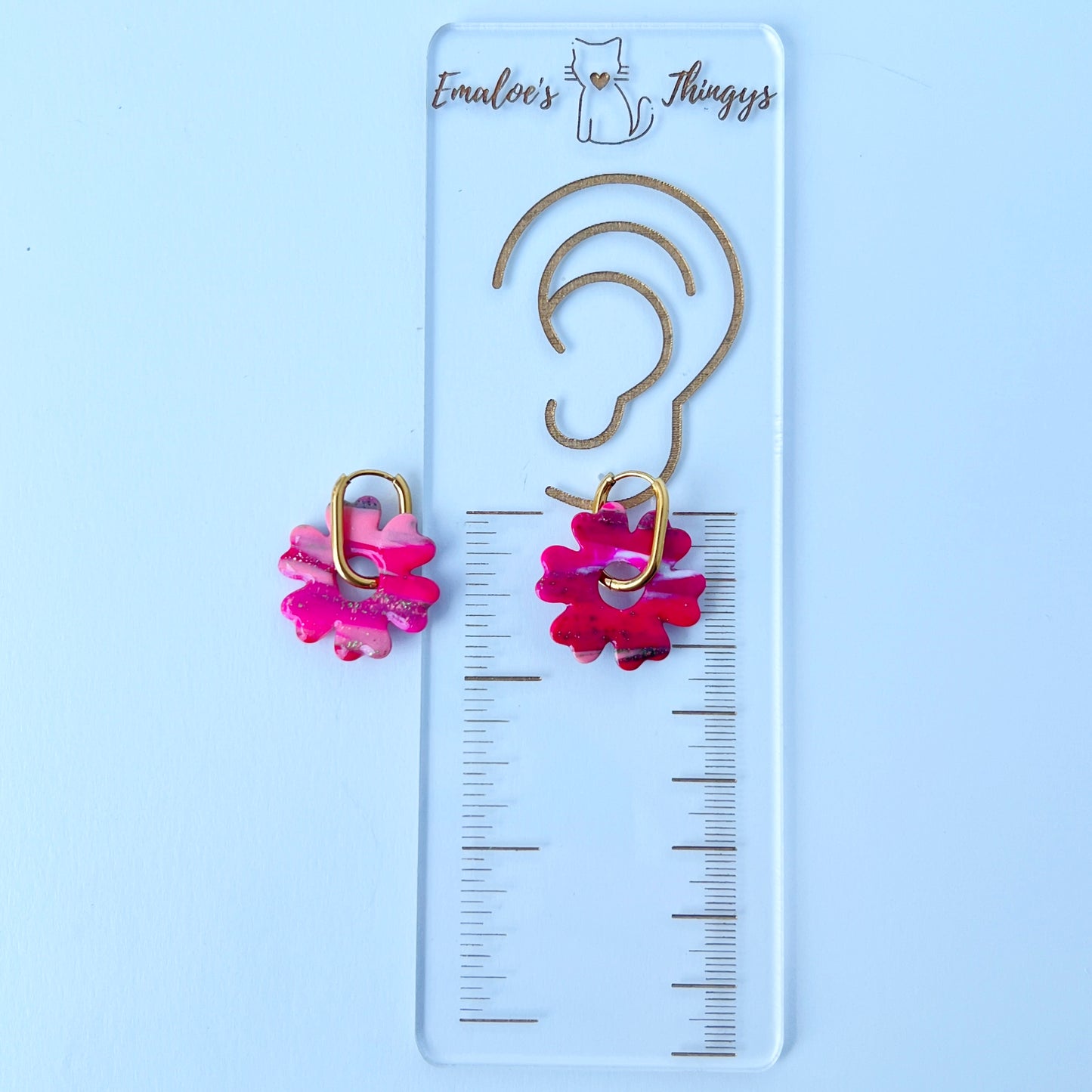 A pair of bold pink handmade polymer clay earrings shaped like abstract flowers, each dangling from a gold oval-shaped 316L stainless steel hoop.
