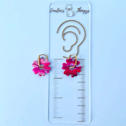 A pair of bold pink handmade polymer clay earrings shaped like abstract flowers, each dangling from a gold oval-shaped 316L stainless steel hoop.