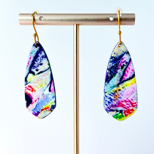 Asymmetrical dagger-shaped earrings made of polymer clay with vibrant marbling that looks like abrushstroke patterns in rainbow colors. Hanging on gold stainless steel earwires.