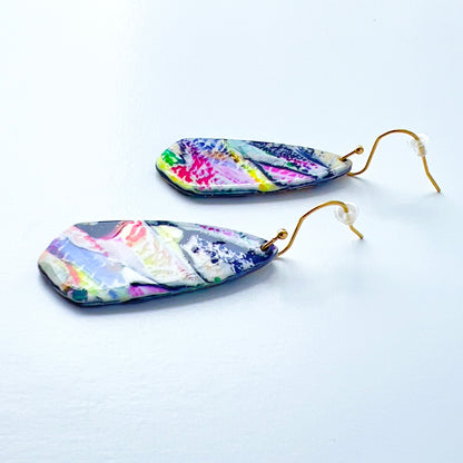 Asymmetrical dagger-shaped earrings made of polymer clay with vibrant brushstroke patterns in rainbow colors. Hanging on gold stainless steel earwires.