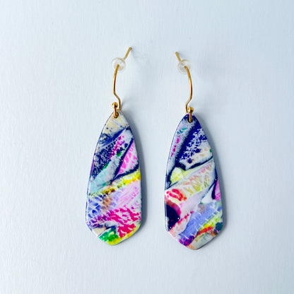 Asymmetrical dagger-shaped earrings made of polymer clay with vibrant marbling that looks like abrushstroke patterns in rainbow colors. Hanging on gold stainless steel earwires.