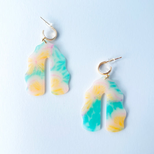 A pair of handmade polymer clay earrings shaped like arches, with swirled pastel colors and subtle details of yellow butterflies and green leafy accents. The semi-transparent clay design is paired with shiny gold-plated brass half hoop posts.