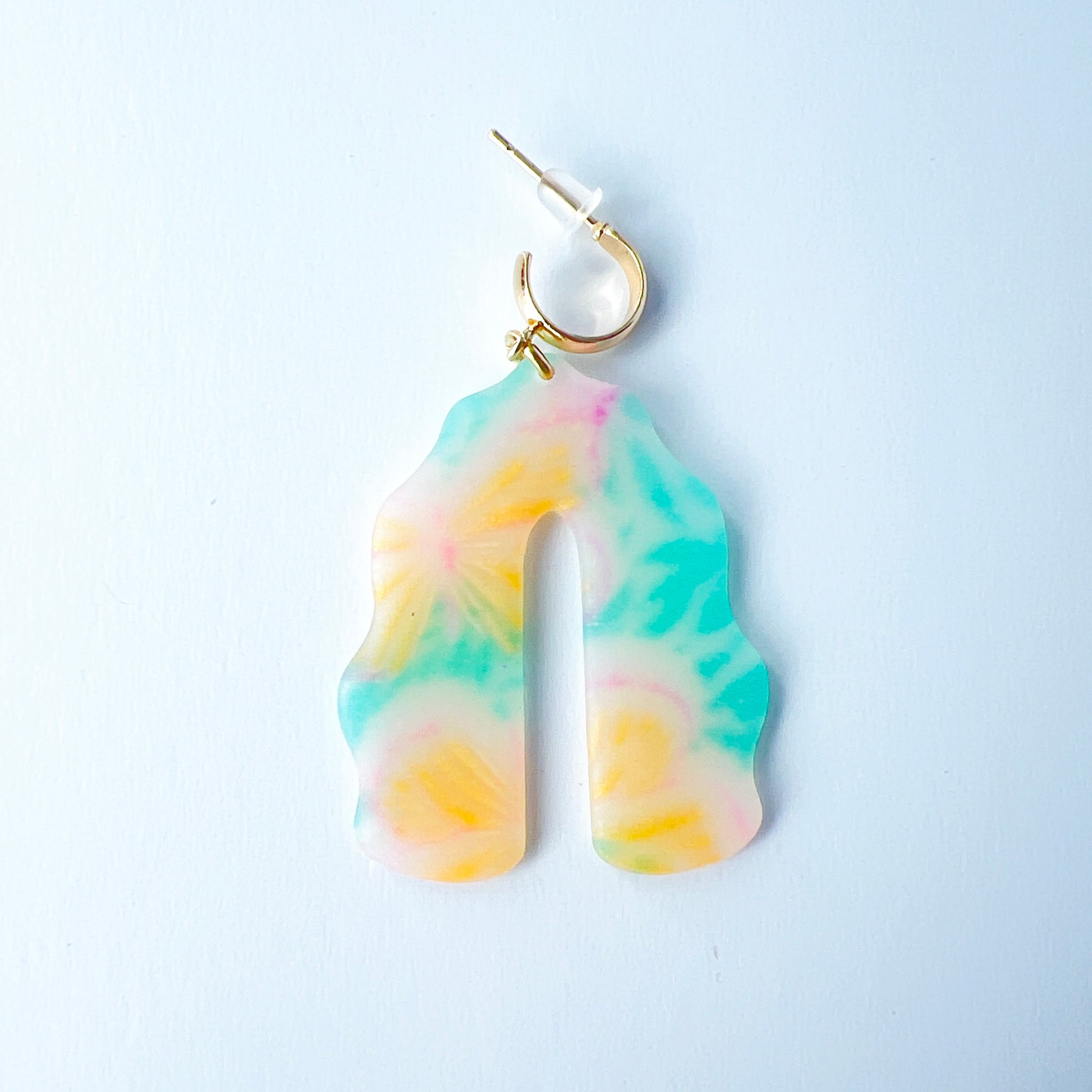 A pair of handmade polymer clay earrings shaped like arches, with swirled pastel colors and subtle details of yellow butterflies and green leafy accents. The semi-transparent clay design is paired with shiny gold-plated brass half hoop posts.