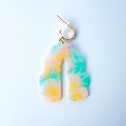 A pair of handmade polymer clay earrings shaped like arches, with swirled pastel colors and subtle details of yellow butterflies and green leafy accents. The semi-transparent clay design is paired with shiny gold-plated brass half hoop posts.