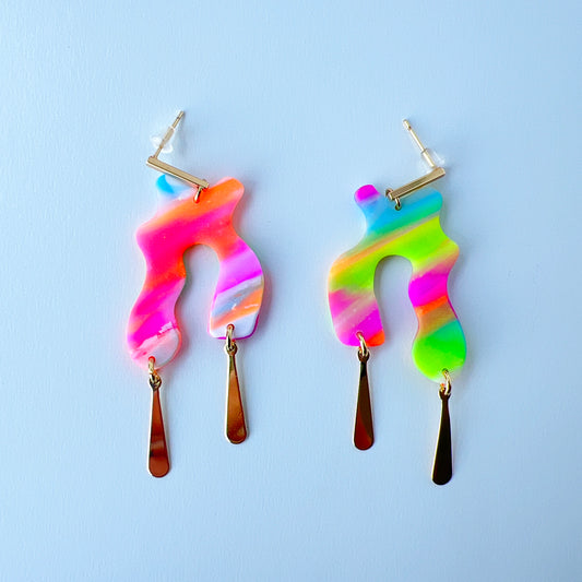 A pair of handmade neon abstract-shaped polymer clay earrings featuring rainbow marbled colors (green, pink, orange, purple, and coral) with shiny gold-plated vertical bar dangles.