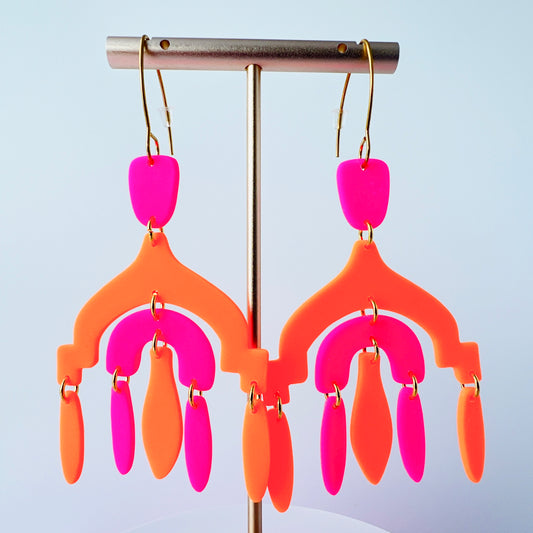 A pair of vibrant handmade chandelier earrings with hot pink and neon orange polymer clay components, featuring multiple dangling shapes on gold-plated stainless steel earwires. 