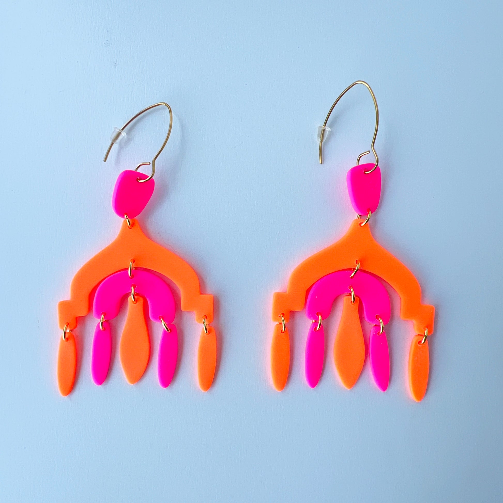 A pair of vibrant handmade chandelier earrings with hot pink and neon orange polymer clay components, featuring multiple dangling shapes on gold-plated stainless steel earwires.