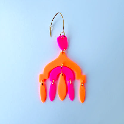 A vibrant handmade chandelier earring with hot pink and neon orange polymer clay components, featuring multiple dangling shapes on gold-plated stainless steel earwires.