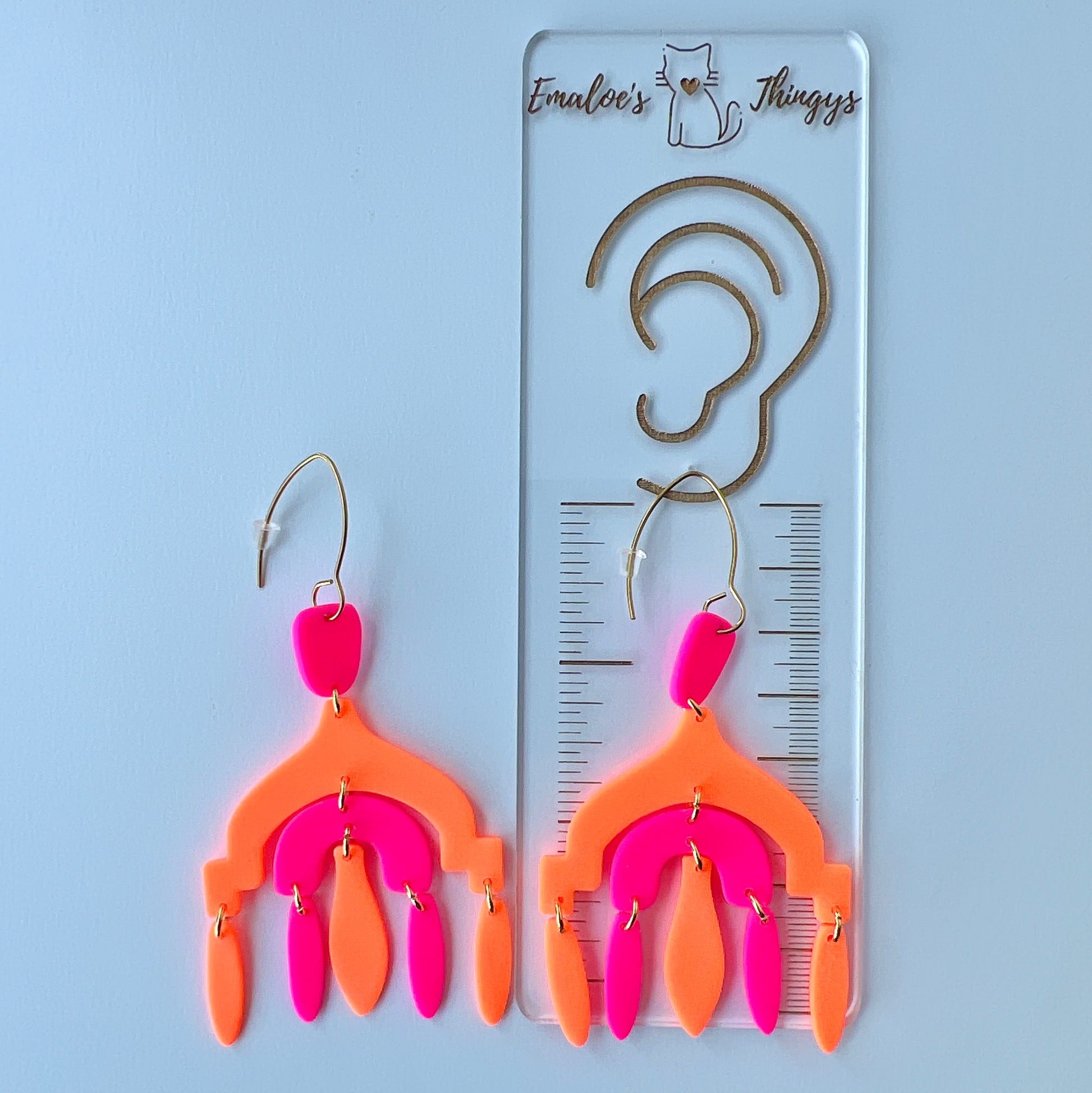 A pair of vibrant handmade chandelier earrings with hot pink and neon orange polymer clay components, featuring multiple dangling shapes on gold-plated stainless steel earwires.