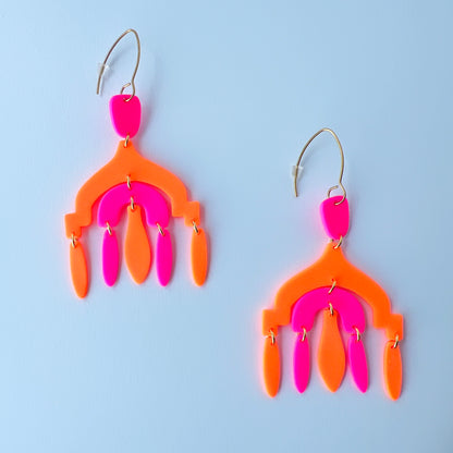 A pair of vibrant handmade chandelier earrings with hot pink and neon orange polymer clay components, featuring multiple dangling shapes on gold-plated stainless steel earwires.