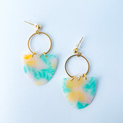 A pair of handmade earrings featuring semi-transparent polymer clay shields with soft pastel patterns of yellow butterflies and green leaves, attached to gold-plated hoops and ball posts.
