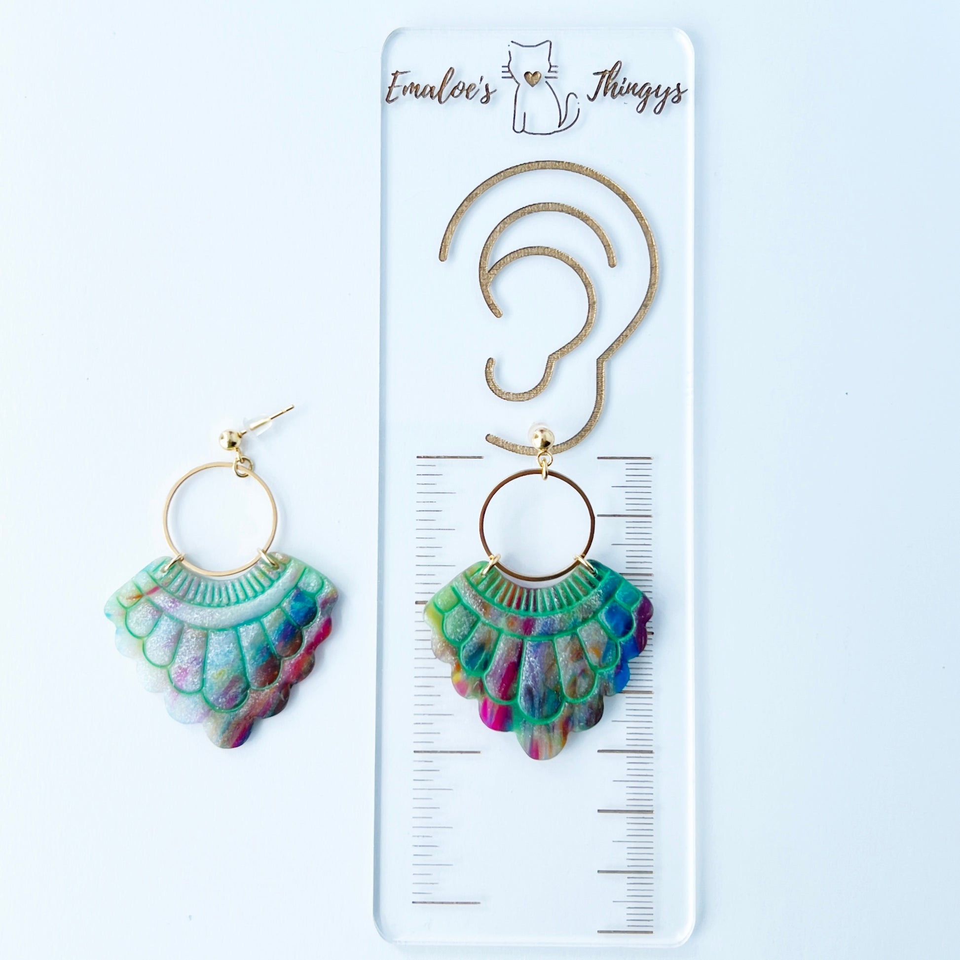 A pair of handmade fan-shaped polymer clay earrings displayed on a white background. The earrings feature gold-plated ball posts and hoops, with semi-transparent rainbow-colored clay and green etched fan-like lines. The marbling effect shows swirls of pink, blue, green, orange, and white.
