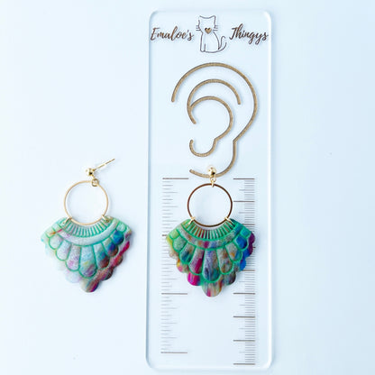 A pair of handmade fan-shaped polymer clay earrings displayed on a white background. The earrings feature gold-plated ball posts and hoops, with semi-transparent rainbow-colored clay and green etched fan-like lines. The marbling effect shows swirls of pink, blue, green, orange, and white.