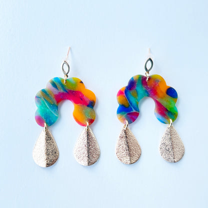 Bold handmade earrings with abstract rainbow swirl polymer clay tops in a semi-translucent finish, featuring glitter-textured gold teardrop dangles and 18K gold-plated brass oval stud posts
