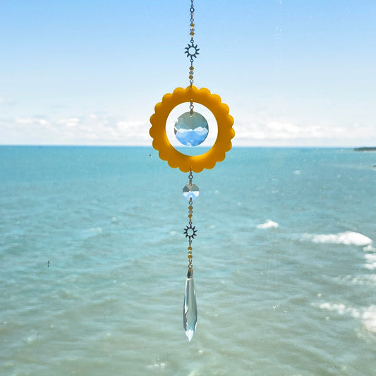 Handmade scalloped-edge circle suncatcher crafted from semi‑translucent pastel polymer clay, suspended from a gold‑plated stainless steel chain and loop. Below the circle hang multiple strands of glass crystal beads, including faceted clear and colored droplets, catching and reflecting light indoors.