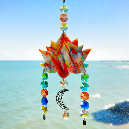 A handmade lotus flower suncatcher crafted from multicolored polymer clay, featuring a stylized lotus bloom suspended from a gold chain with a faceted glass crystal hanging below, designed to reflect rainbow light in the sun. Ideal for meditation rooms, spiritual decor, or peaceful window displays.