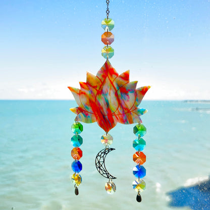 A handmade lotus flower suncatcher crafted from multicolored polymer clay, featuring a stylized lotus bloom suspended from a gold chain with a faceted glass crystal hanging below, designed to reflect rainbow light in the sun. Ideal for meditation rooms, spiritual decor, or peaceful window displays.