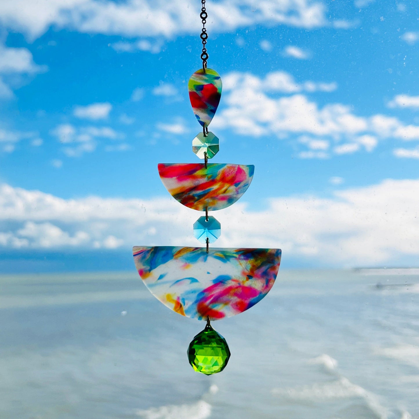 Watercolor: Soft marbled polymer clay suncatcher in oceanic tones of pink, blue, yellow, and green, with green and aqua crystal accents and gold chain.