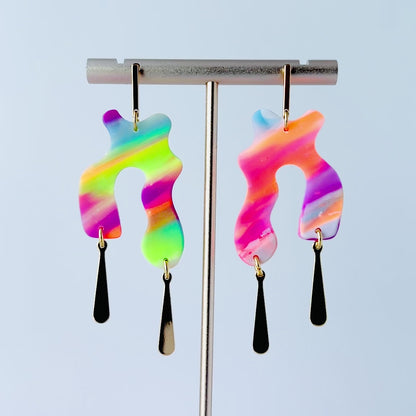 Video of a pair of handmade neon abstract-shaped polymer clay earrings featuring rainbow marbled colors (green, pink, orange, purple, and coral) with shiny gold-plated vertical bar dangles. 