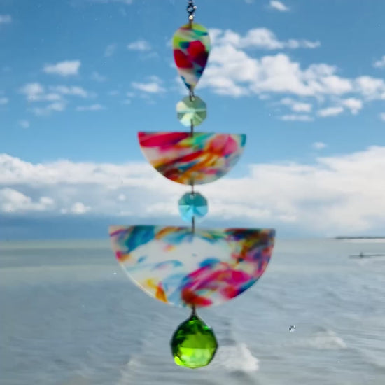 video of Watercolor: Soft marbled polymer clay suncatcher in oceanic tones of pink, blue, yellow, and green, with green and aqua crystal accents and gold chain.