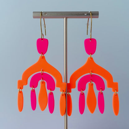 Video of a pair of vibrant handmade chandelier earrings with hot pink and neon orange polymer clay components, featuring multiple dangling shapes on gold-plated stainless steel earwires.