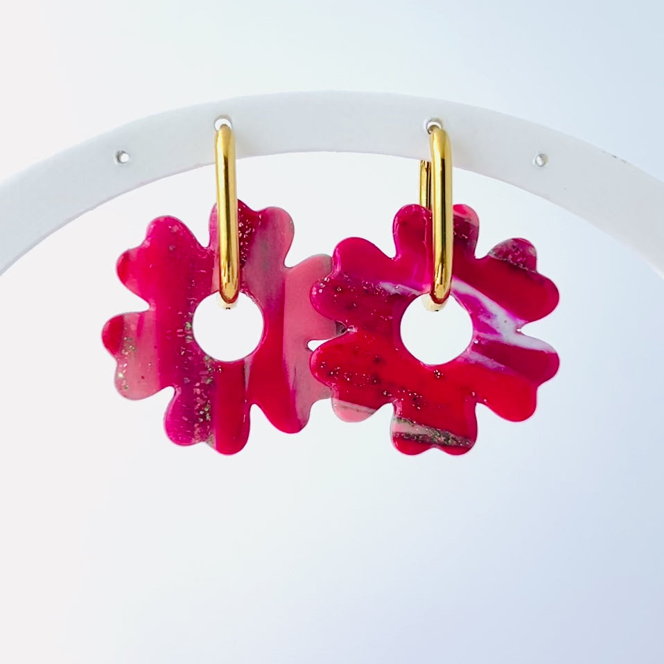 Video of s pair of bold pink handmade polymer clay earrings shaped like abstract flowers, each dangling from a gold oval-shaped 316L stainless steel hoop. 