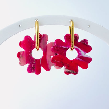 Video of s pair of bold pink handmade polymer clay earrings shaped like abstract flowers, each dangling from a gold oval-shaped 316L stainless steel hoop. 