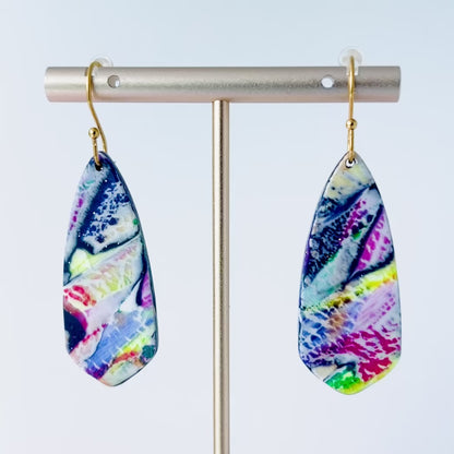 Video of a pair of asymmetrical dagger-shaped earrings made of polymer clay with vibrant marbling that looks like brushstroke patterns in rainbow colors. Hanging on gold stainless steel earwires.